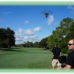 Professional drone pilot operating equipment beside a golf course